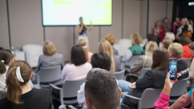 Business professional giving a presentation to attentive audience in modern conference setup setting.