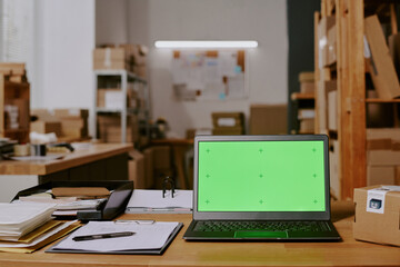 Organized office storage space with laptop showing green screen on desk equipped with office supplies and documents scattered around