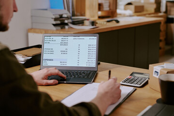 Person inputting financial details on laptop while calculating expenses with calculator. Office...