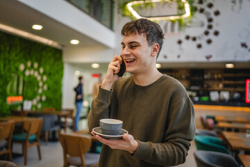 young man student hold cup of coffee and talk on mobile phone at cafe