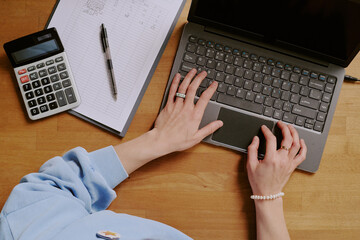 Hands seen typing on laptop with nearby notepad, pen, and calculator, demonstrating multitasking...