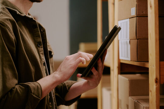 Young man checking inventory on shelves using tablet in warehouse setting highlighting efficiency and modern technology implementation for stock management