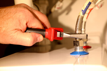 Naklejka premium Using pliers, an experienced and professional plumber connects hot and cold water hoses to a boiler.