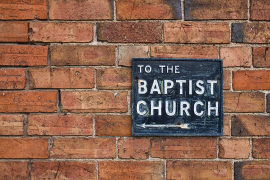 Vintage, Victorian sign with cracked white road font lettering and with an arrow, set against red brick wall showing direction for the Baptist Church in Stratford-upon-Avon, England