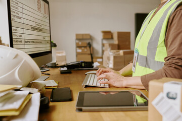 Worker in high-visibility vest scanning packages in storage room with boxes, electronic devices and storage shelves visible in background
