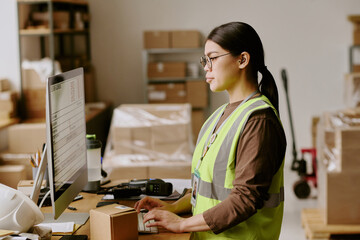 Employee handling package in warehouse, managing inventory using computer system and barcode...