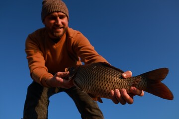 Fisherman holding caught fish against blue sky, low angle view