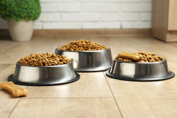 Dry pet food in feeding bowls and chew bones on floor indoors