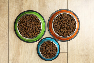 Dry pet food in feeding bowls on wooden floor, flat lay