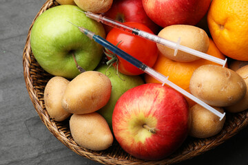 GMO concept. Different products and syringes in basket on grey textured table, top view