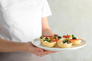 Woman holding plate with tasty canapes on light grey background, closeup