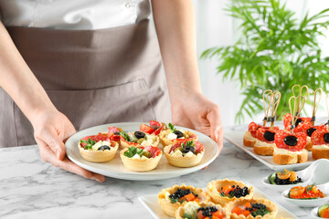 Woman with many different tasty canapes at white marble table, closeup