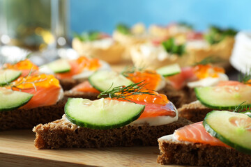 Tasty canapes with salmon and cucumber on wooden board, closeup