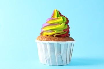 One delicious cupcake with colorful cream on light blue background, closeup