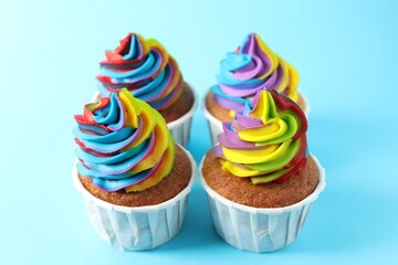 Delicious cupcakes with colorful cream on light blue background, closeup