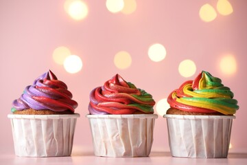 Delicious cupcakes with colorful cream on table against pink background, closeup and space for text. Bokeh effect