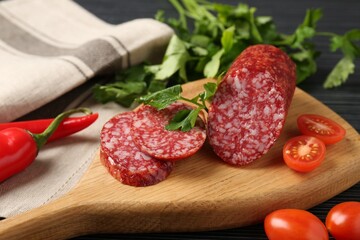 Cut smoked sausage, parsley and tomatoes on black wooden table, closeup