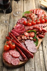 Different smoked sausages, tomatoes, ham and wine on wooden table, closeup