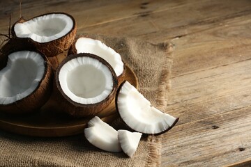 Pieces of cracked coconuts on wooden table, closeup. Space for text