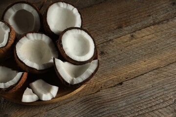Pieces of cracked coconuts on wooden table, closeup. Space for text