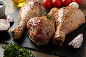 Raw marinated turkey drumsticks and products on wooden table, closeup