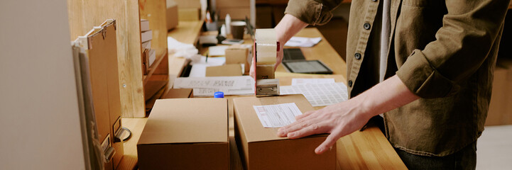 Worker sealing boxes with a packing tape machine in warehouse environment showing organized...
