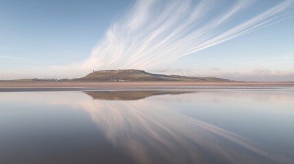 Serene coastal landscape with hill reflecting in calm water under a vibrant sky.