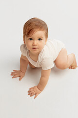 Aerial view of playful baby, dressed white onesie, crawling forward with bright eyes focused ahead...