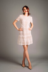 Studio candid portrait of ginger woman in white mesh dress on high heels. Transparent midi short sleeve gown. Beautiful makeup with red lips and natural bun hairdo with curls. Feminine bridal fashion