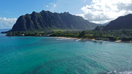 Fototapeta premium Kualoa Mountains and turquoise ocean, scenic Hawaiian coastline with lush greenery and sandy beach.