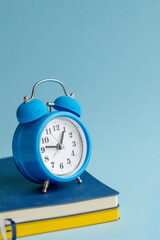 The blue alarm clock stands on the diaries in blue and yellow on a blue background. Side view. Vertical photography