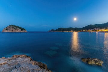Moonlit coastal scene, island, calm sea, village lights, tranquil night