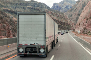 Truck driving down mountain road, surrounded by lush green trees and vast stretches of nature under...