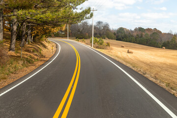 Fototapeta premium Road with yellow lines cutting through a dense forest, sunlight filtering through the branches creating dappled shadows on the pavement.