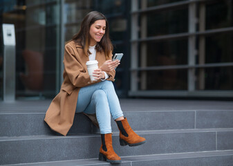 Businesswoman using smartphone and drinking coffee outdoors