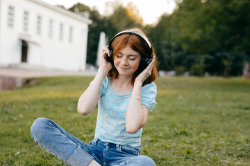 Teenage girl listening to music in wireless headphones with eyes closed while sitting on the grass