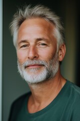 Obraz premium A man with a beard and gray hair is smiling at the camera. He is wearing a green shirt