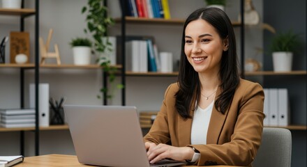 Fototapeta premium A professional and young businesswoman with long dark hair and a warm smile working on her laptop in a modern office setting