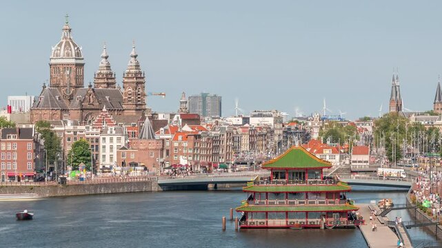 Aerial cityscape panorama with the Basilica of Saint Nicholas in Amsterdam's Old Centre near the Central Station timelapse. People walking along the waterfront by boat station. Amsterdam, Netherlands