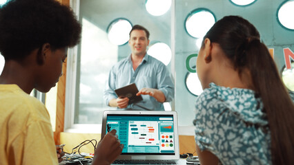 Smart teacher hold tablet while back view student learning engineering code on table with laptop...