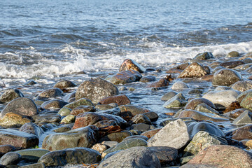 Waves crash against rocks on a rocky beach, some of the rocks have been washed by the water and turned into pebbles