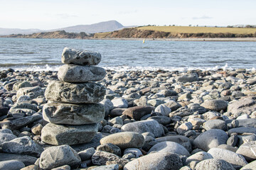 A pyramid of large stones on a rocky beach, with the sea in the background and a green island behind it.