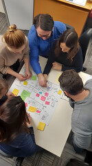 Top view of a diverse team of members gathered around a table, with a flowchart and sticky notes displayed
