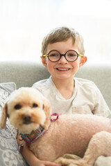 portrait of handsome little boy in glasses sit on sofa with dog
