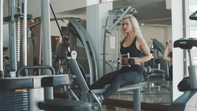 Strong woman demonstrates slow motion rowing exercise in gym setting