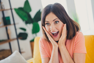 Fototapeta premium Joyful young woman with brunette bob hairstyle expressing excitement in bright living room interior with trendy decor
