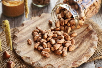 Shelled hazelnuts spilled from a glass jar, with a jar of nut butter in the background