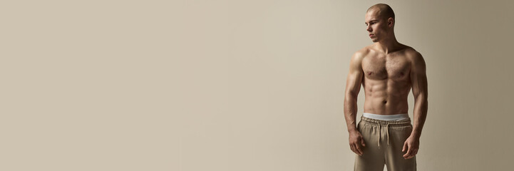 Banner. Athletic man standing with calm expression, gaze downward, muscular physique emphasized by...