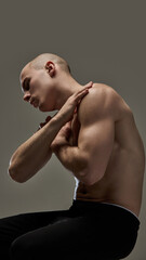 Fit man embracing own shoulder, highlighting sculpted muscles and tension in pose against...