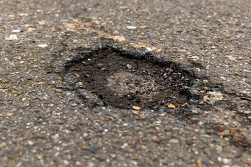Pothole on a city street revealing damaged asphalt and debris in the afternoon sunlight